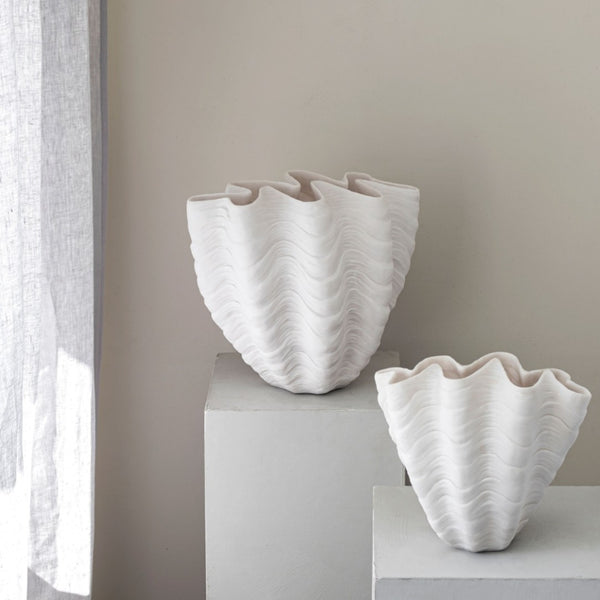 Two white textured vases on a light surface with a neutral background