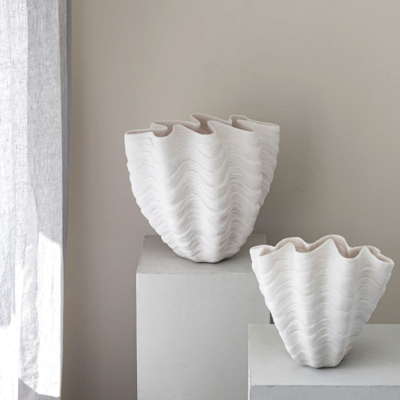 Two white textured vases on a light surface with a neutral background
