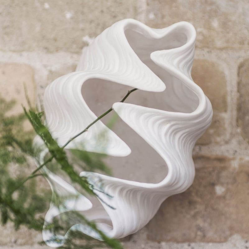 White ceramic vase with wavy design on a textured beige surface