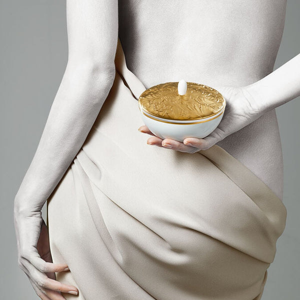 Person holding a gold and white sugar pot in porcelain with a neutral background