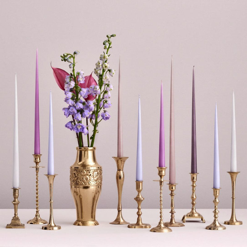 Decorative setup with candles in brass candlesticks and a gold vase with flowers on a light background