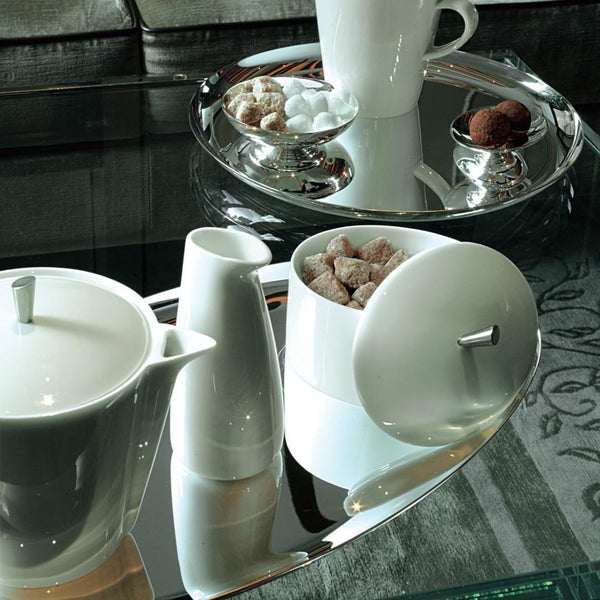 White ceramic tea set on a reflective surface with a blurred background