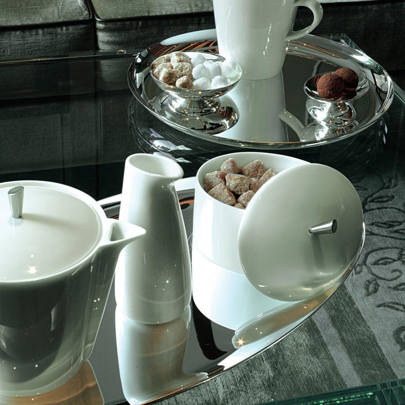 White ceramic tea set on a reflective surface with a blurred background