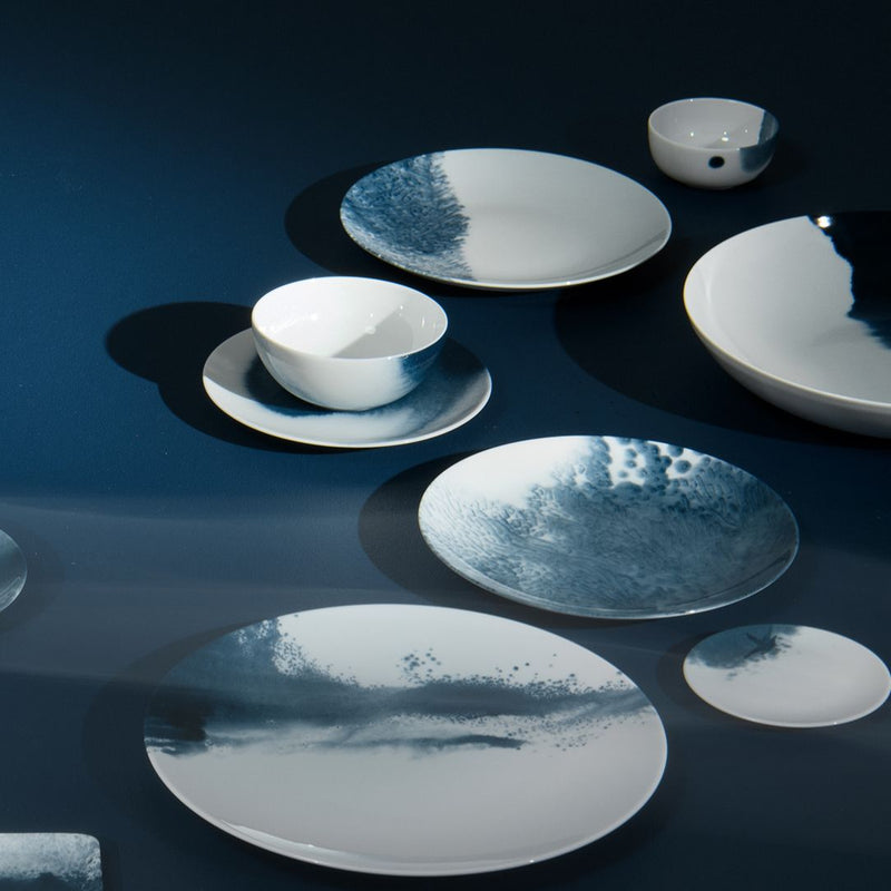 Set of white ceramic plates and bowls with blue accents on a dark reflective surface