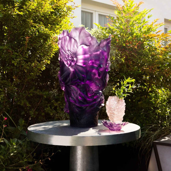 Purple floral sculpture on a round metal table with greenery in the background