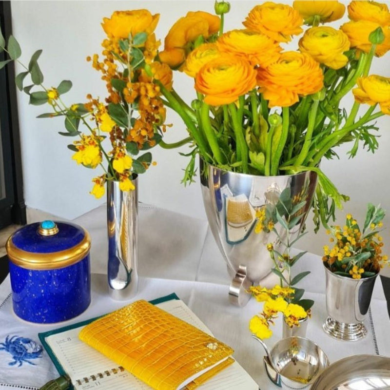 Decorative table setting with yellow flowers, a blue container, and silver vases.