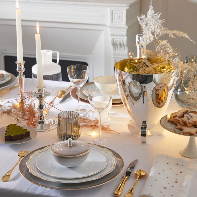 Elegant table setting with gold and white decor, including candles and a cake, in a room with a fireplace.