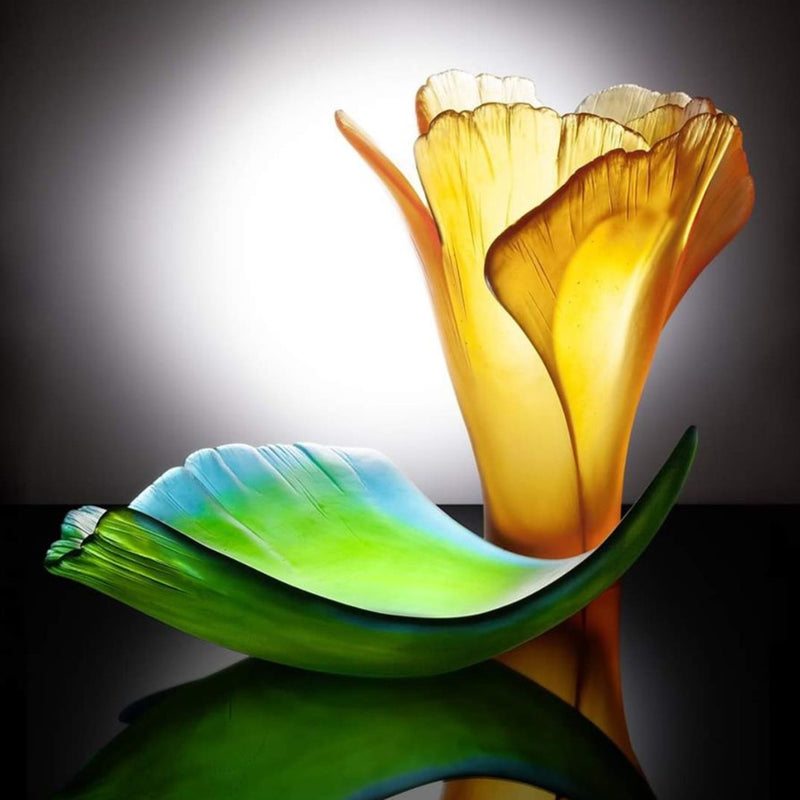 Artistic glass sculpture of a flower with green and orange colors on a dark background