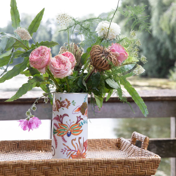 Floral arrangement in a decorated vase on a woven surface with a blurred natural background