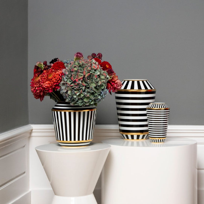 Black and white striped vases with flowers on a white surface against a gray wall.
