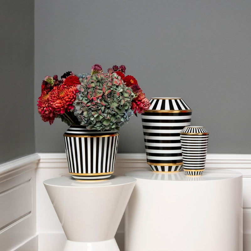 Black and white striped vases with flowers on a white surface against a gray wall.