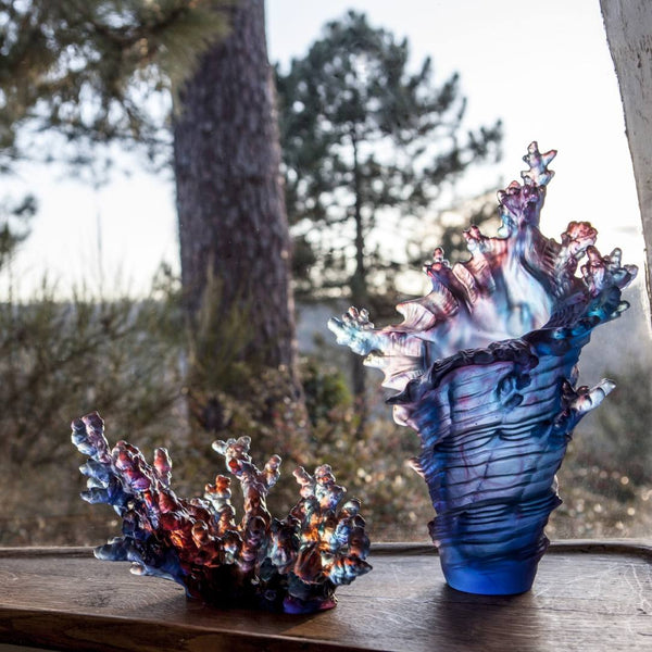 Two glass coral shape sculptures on a wooden surface with a natural background