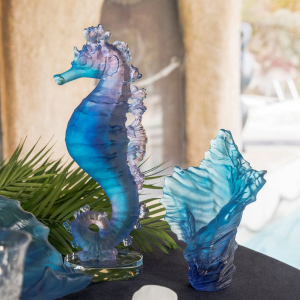 Blue glass seahorse and sea urchin figurines on a dark surface with green leaves.