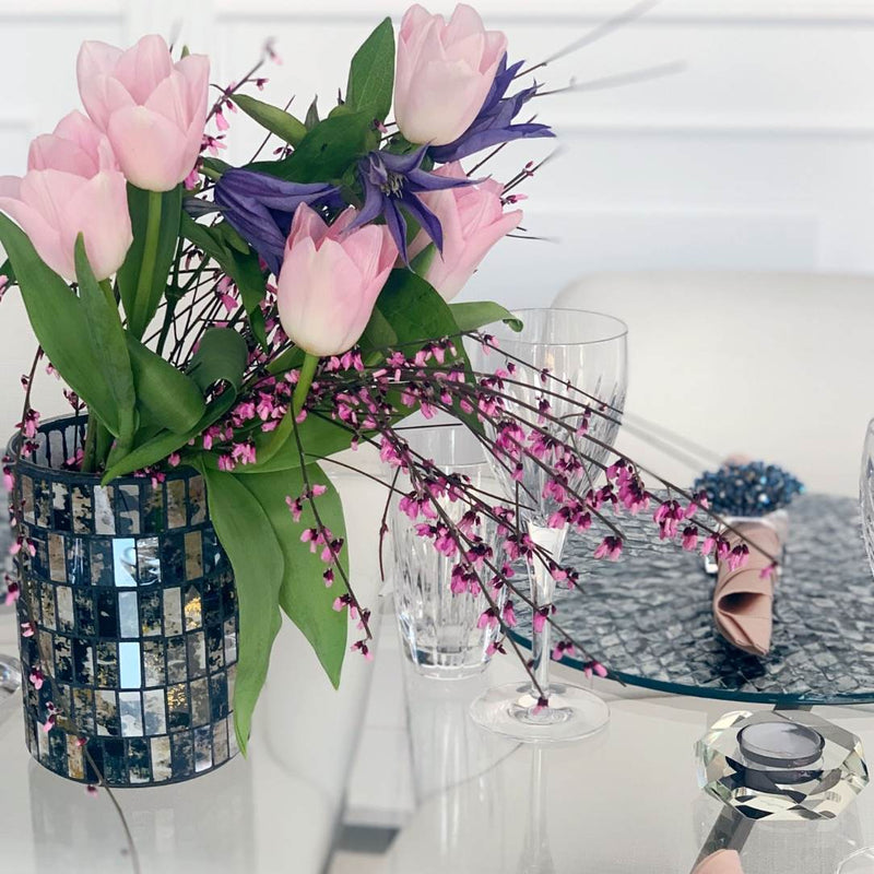 Decorative table setting with pink tulips in a mosaic vase, wine glasses, and a candle.