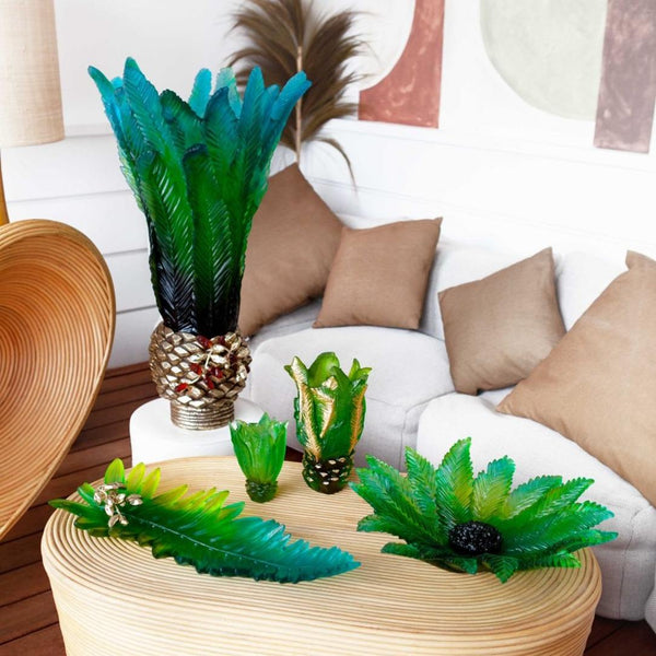 Decorative green plants in gold and green vases on a wooden table with a white sofa and pillows in the background.