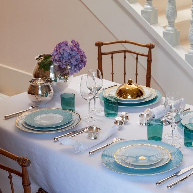 Elegant table setting with blue and gold plates, silverware, and glasses on a white tablecloth.