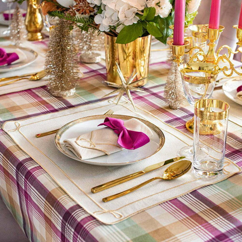 Elegant table setting with gold cutlery, pink napkin, and floral centerpiece on a plaid tablecloth.