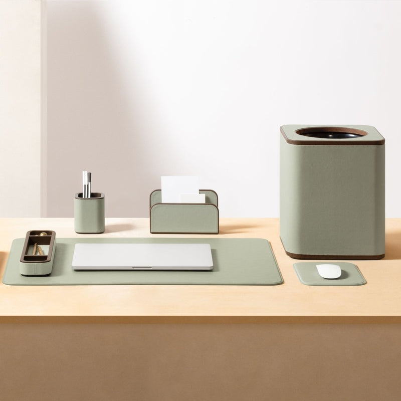 Desk setup with green office accessories including a trash can, paper holder, and mouse pad on a light wooden surface.
