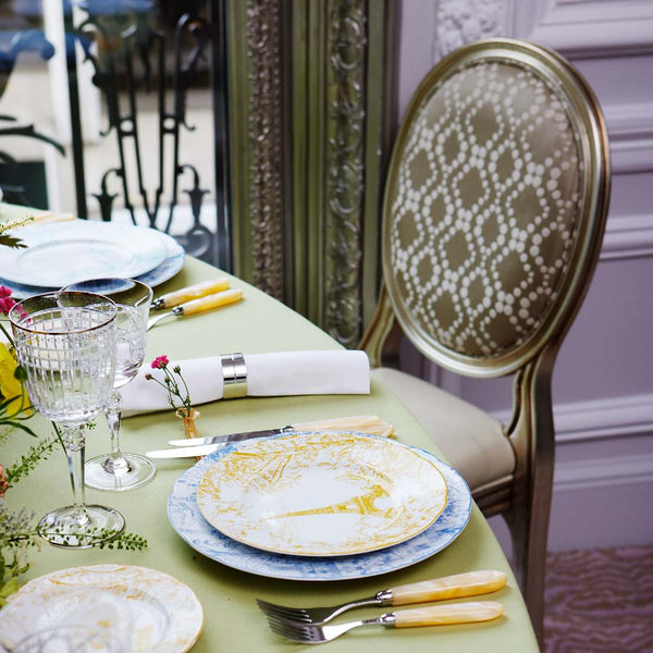 Elegant table setting with plates, Aghata glasses, and cutlery on a green tablecloth.