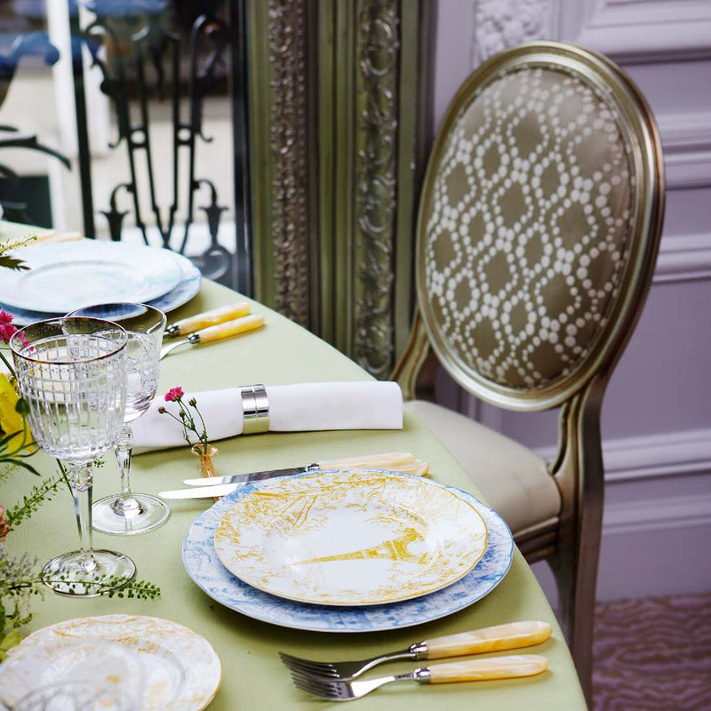 Elegant table setting with plates, Aghata glasses, and cutlery on a green tablecloth.