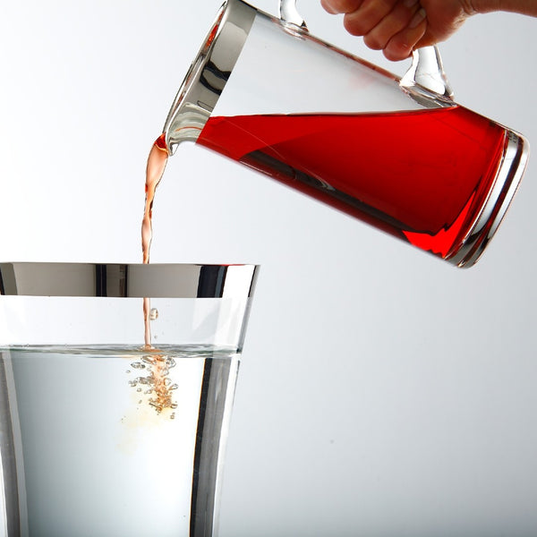 Red liquid being poured from a glass carafe Basby by Sonja Quandt into another container on a white background