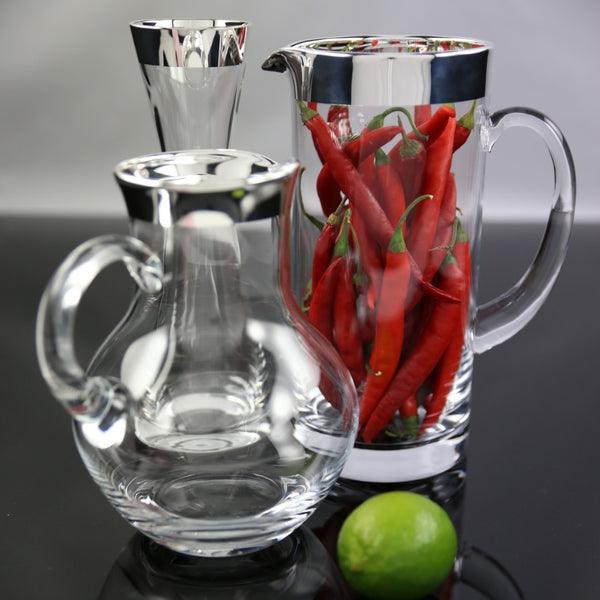 Clear glass pitchers with red chilies and a lime on a reflective surface