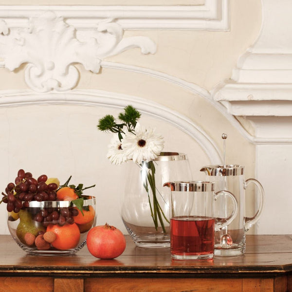 Fruits, flowers, and a pitcher with 2cm Fine Silver Rim – Paris Collection by Sonja Quandt on a wooden surface with decorative wall molding.