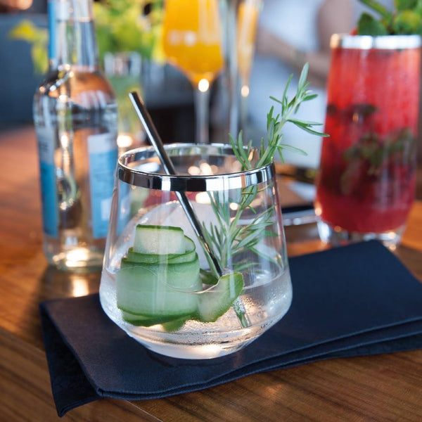 Elegant Crystal Whisky Glass with Hand-Applied Silver Rim – Avantgarde by Sonja Quandt with cucumber slices and rosemary on a wooden table with other drinks in the background