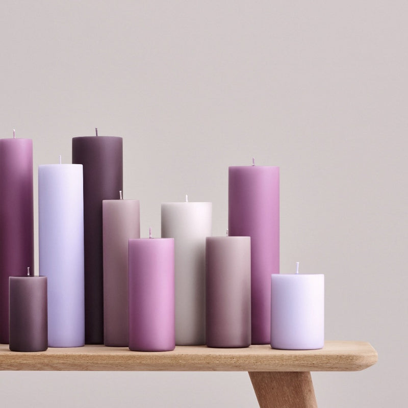 Row of purple and pink candles on a wooden surface with a light gray background