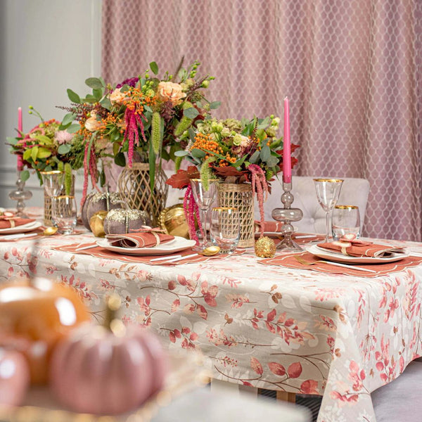 Decorative table setting with floral centerpieces, candles, and pumpkins on a patterned tablecloth.