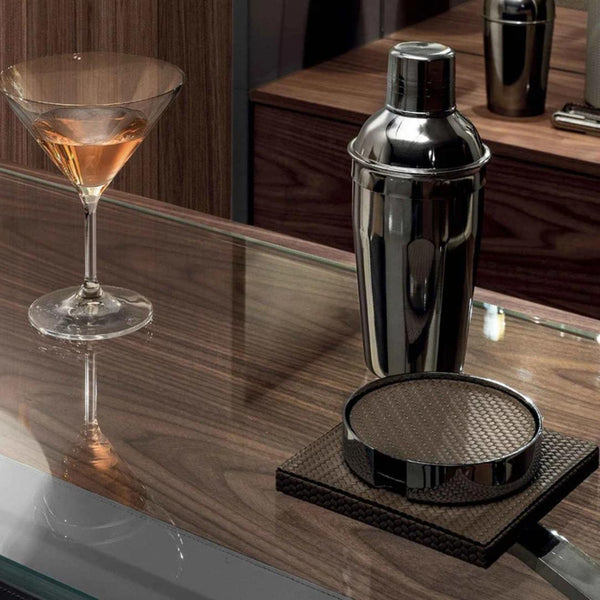Silver cocktail shaker on a wooden bar with a glass of cocktail and the woven Pinetti Coaster set.