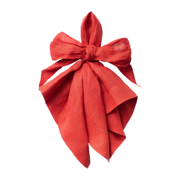 Pre-tied red linen napkin in a bow shape by Joanna Buchanan on white background.