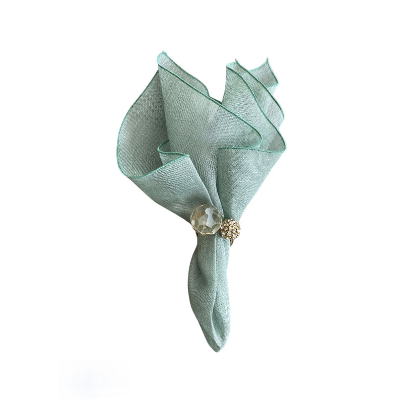 Garza linen gauze napkin in sage green styled with shiny gold napkin ring top view, sold at Amiramour.