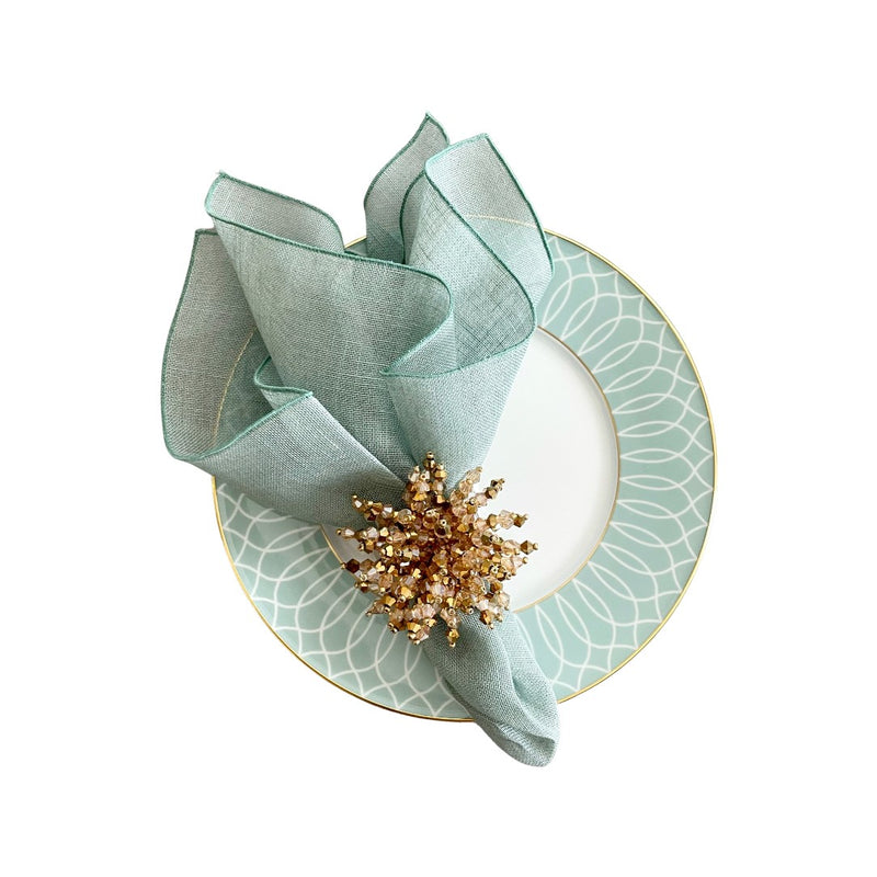 Garza linen gauze napkin in sage green styled with shiny gold napkin ring on porcelain green plate, sold at Amiramour.