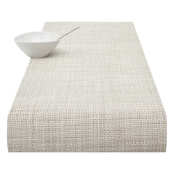 A natural-colored basketweave table runner with a textured surface, displayed on a white background alongside a white bowl for scale.