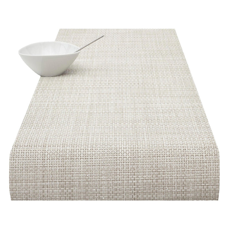 A natural-colored basketweave table runner with a textured surface, displayed on a white background alongside a white bowl for scale.
