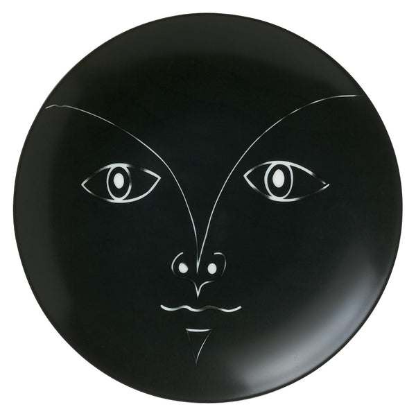 A black porcelain bread plate featuring a stylized human face design, inspired by the works of Jean Cocteau.