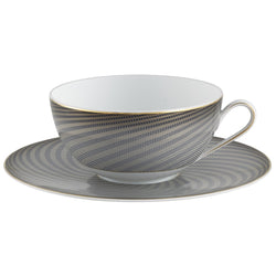 A white porcelain breakfast cup with black and gold geometric patterns on the cup and saucer, held by a gold-colored handle.