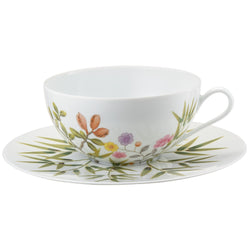 A white porcelain cup and saucer with green, brown, and pink floral patterns and turquoise accents.