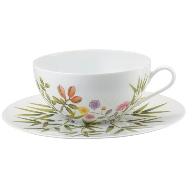 A white porcelain cup and saucer with green, brown, and pink floral patterns and turquoise accents.