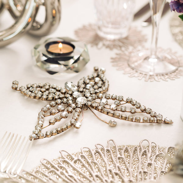 Bejewelled butterfly figurine with clear crystals styled on a white tablecloth with a candle in the back