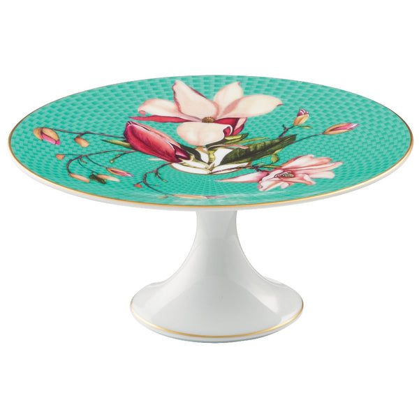 A small round porcelain cake stand with a floral pattern, featuring colors such as beige, chestnut, gold, and turquoise. The stand has a white base and gold accents around the edge.