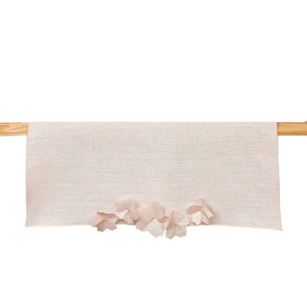 A light pink linen table runner with cherry blossom embellishments, displayed on a wooden table.