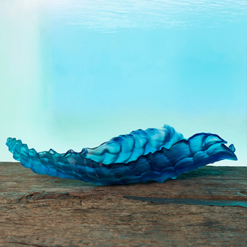 A blue crystal centerpiece sculpture with a wavy, coral-like pattern on a wooden console and sea like background