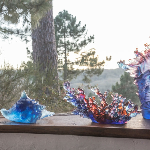 A sculpted crystal coral bowl and seashell in blue and amber colors with a solid pattern.