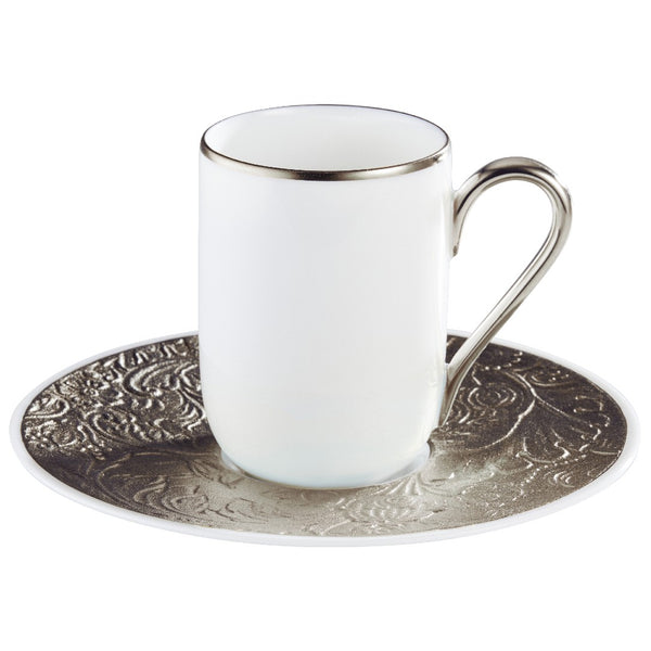 A white porcelain espresso cup with a platinum rim and a saucer with detailed platinum engravings.