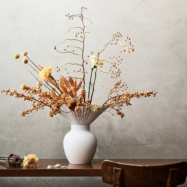 styled falda vase in white with flowers against a grey textured wall