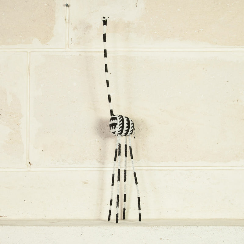 A decorative giraffe sculpture with a black and white color scheme, featuring traditional wire and glass beadwork with cream background