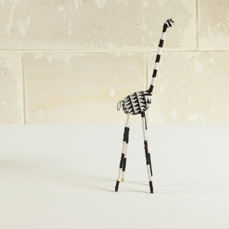 A decorative giraffe sculpture with a black and white color scheme, featuring traditional wire and glass beadwork on cream background