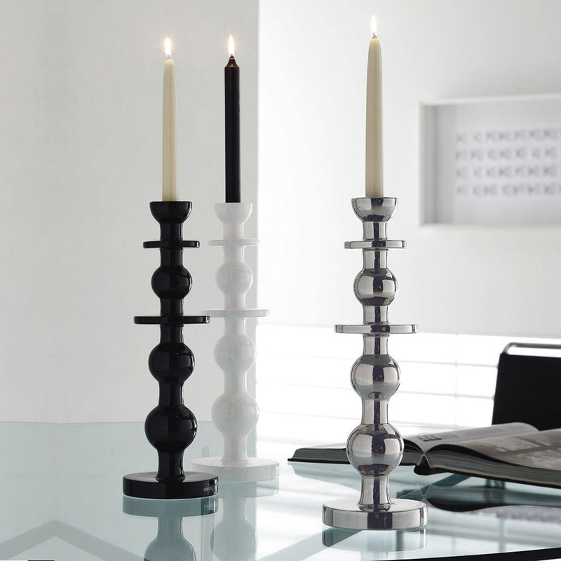 Contemporary black glazed ceramic candle holders by Adriani e Rossi, shown holding lit candles, placed on a glass surface.